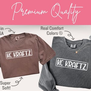 May include: Two t-shirts, one brown and one gray, with the text "KC KRAFTZ" in a white rectangle. The brown shirt is short-sleeved, and the gray shirt is long-sleeved. The image includes the text "Printed in the USA," "Real Comfort Colors," and "Super Soft!"