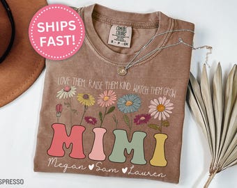 May include: A brown t-shirt with a floral design and the text "Love them, raise them kind, watch them grow" above the word "MIMI" in colorful letters. The names "Megan, Sam, Lauren" are written below the word "MIMI".