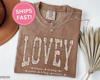 May include: A brown t-shirt with the word "LOVEY" spelled out in floral letters. The names "Megan, Sammy, James, Kelsey, Connor" are written below the word "LOVEY" in a smaller font.