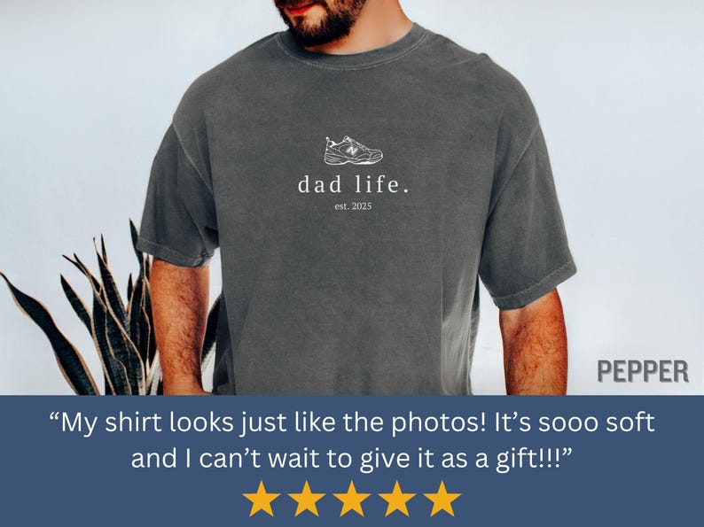 May include: A dark gray t-shirt with a white graphic of a sneaker and the text "dad life. est. 2025".
