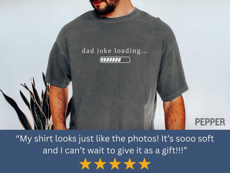 May include: Dark gray t-shirt with the text "dad joke loading..." and a loading bar graphic. The shirt is a casual style, suitable for everyday wear. The word "PEPPER" is in the upper right corner.