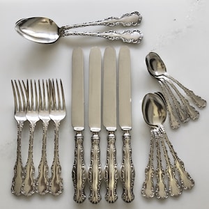 May include: A set of silverware featuring five forks, five spoons, and five knives. The silverware is made of polished silver and has an ornate design.