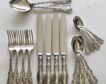May include: A set of silverware featuring five forks, five spoons, and five knives. The silverware is made of polished silver and has an ornate design.