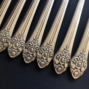 Peut inclure: Gros plan de plusieurs fourchettes argentées. Les manches sont décorés d'un motif floral de roses. Les fourchettes sont disposées en diagonale sur un fond sombre, mettant en valeur les détails de l'argenterie.