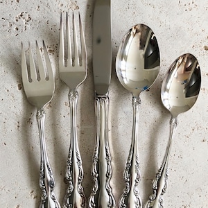 May include: Set of five silver-plated cutlery pieces, including a knife, fork, and three spoons. The pieces have an ornate, floral design.