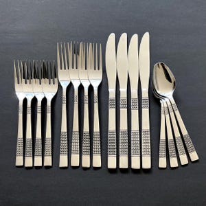 May include: A set of stainless steel flatware, including forks, knives, and spoons, arranged on a dark surface. The silverware features a decorative pattern on the handles. The set includes multiple forks, knives, and spoons.