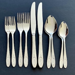Peut inclure: Un ensemble d'argenterie polie, comprenant des fourchettes, des couteaux et des cuillères, disposé sur une surface sombre. Les couverts présentent un motif floral décoratif sur les manches. L'ensemble comprend plusieurs fourchettes, couteaux et cuillères.