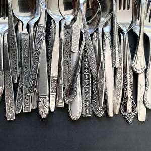 May include: A white ceramic mug with a black handle and the text "But First, Coffee" in a bold, black font. The mug is set against a blurred background, suggesting a cozy setting. The mug appears to be approximately 4 inches tall.