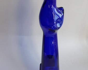 Può includere: Una bottiglia di vetro blu cobalto a forma di gatto. La bottiglia ha un collo rotondo e una base larga. Il viso del gatto è visibile sul davanti della bottiglia.