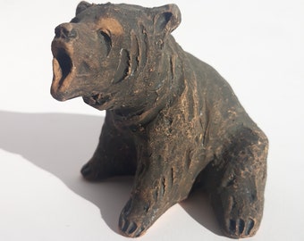 May include: A small, brown ceramic bear figurine with a textured surface. The bear is sitting with its mouth open, as if it is roaring.