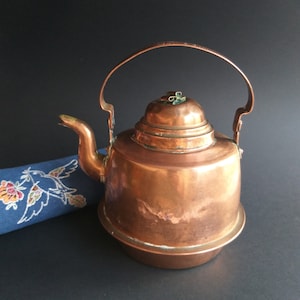 May include: A copper teapot with a rounded body and a lid with a small green knob. The teapot has a curved handle and a spout.