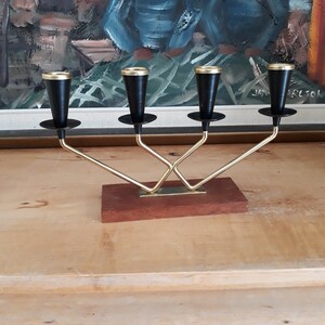 May include: A gold metal candle holder with four black candle cups. The holder has a wooden base.
