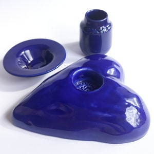May include: A set of three blue ceramic dishes. The largest dish is heart-shaped with a small indentation in the centre. The second largest dish is a round plate with a slight indentation in the centre. The smallest dish is a small vase with a rounded base.