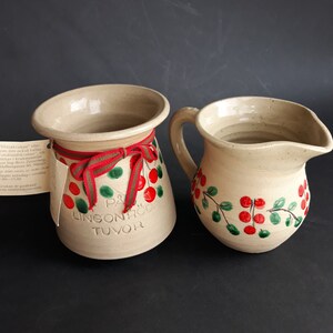 Può includere: Due brocche in ceramica con un motivo floreale rosso e verde. La brocca più grande ha il testo "PA LINGONRODA TUVOR" sul davanti.