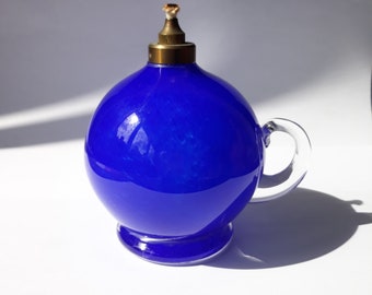 May include: A blue glass oil lamp with a clear glass handle and a brass top.