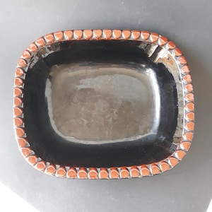 Pode incluir: Um prato quadrado de cerâmica preta com uma borda ondulada marrom. O prato é esmaltado e tem um acabamento brilhante.