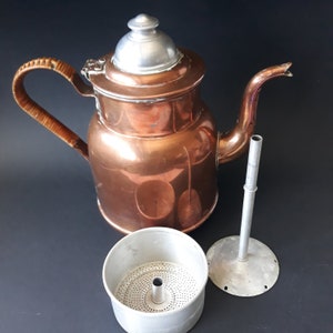Könnte beinhalten: Eine antike Kaffeekanne aus Kupfer mit einem Holzgriff und einem silbernen Deckel. Die Kanne hat einen herausnehmbaren Filter und einen Sockel.