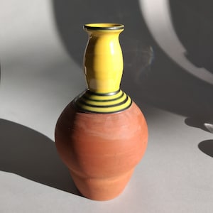 Könnte beinhalten: Eine Terrakotta-Vase mit einem gelben und schwarzen gestreiften Hals. Die Vase hat einen runden Körper und einen schmalen Hals.