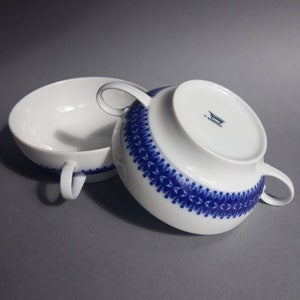 Könnte beinhalten: Zwei weiße Porzellansuppenbowlen mit blau-weißem Muster. Die Schalen haben zwei Henkel und sind übereinander gestapelt. Die untere Schale hat ein blau-weißes Logo mit der Aufschrift "S. Bayern"