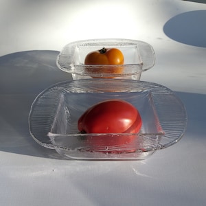 May include: Two clear glass bowls with textured edges, one containing a red tomato and the other a yellow tomato.