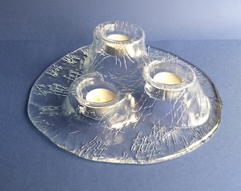 May include: A clear glass candle holder with three individual candle cups. The holder has a textured, cracked glass design.