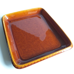 Op de afbeelding: Een rechthoekige serveerschaal van bruin keramiek met een decoratieve rand. De schaal is geglazuurd en heeft een glanzende afwerking.