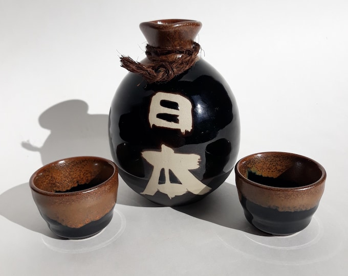 Japanese Kanewake Sake Set of 3 Pieces. Decanter and 2 Cups in Brown, Black Colour Glaze. White Hieroglyphs on Side. Marked Made in Japan.