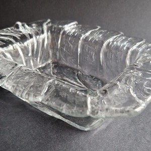 May include: A clear glass dish with a textured, wavy design. The dish is rectangular and has a slightly rounded bottom.