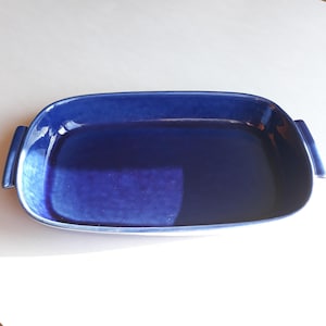 May include: A blue ceramic baking dish with two handles. The dish is oval shaped and has a smooth, glossy finish.