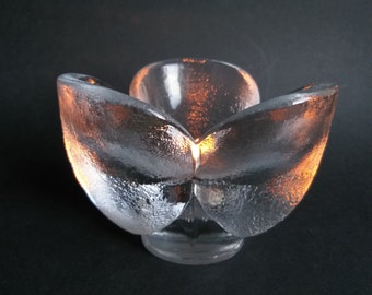 May include: A clear glass candle holder shaped like a flower with five petals. The candle holder is lit and the light shines through the glass.