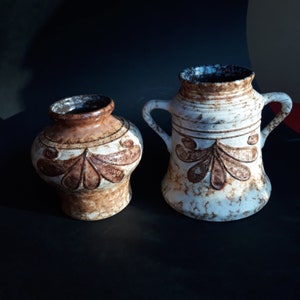 Könnte beinhalten: Zwei Keramikvasen mit brauner und weißer Glasur und einem floralen Design. Die größere Vase hat zwei Henkel.