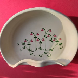 May include: A white ceramic dish with a scalloped edge features a hand-painted design of pink flowers and green leaves.