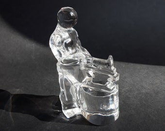 May include: A clear glass sculpture of a person sitting on a stool. The sculpture is detailed and intricate, with a realistic depiction of the person's body and clothing.