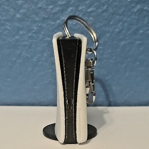 May include: A white and black keychain shaped like a video game console. The keychain has a silver ring and a black clip.