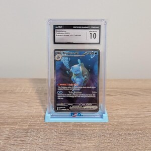 May include: A graded Pok&eacute;mon card featuring Blastoise ex from the Scarlet & Violet 151 set. The card is encased in a protective holder with a Gem Mint 10 grade. The card has a blue and white color scheme, with the Blastoise character in the center.