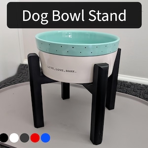 May include: A dog bowl stand with a two-tone ceramic bowl in mint green and cream, accented with black dots. The bowl sits on a black wooden stand. The text "LIVE, LOVE, BARK." is printed on the bowl. The text "Dog Bowl Stand" is in a black rectangle.