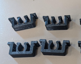 May include: Four black plastic cable clips, each with a U-shaped design, are arranged in two rows on a light brown surface.