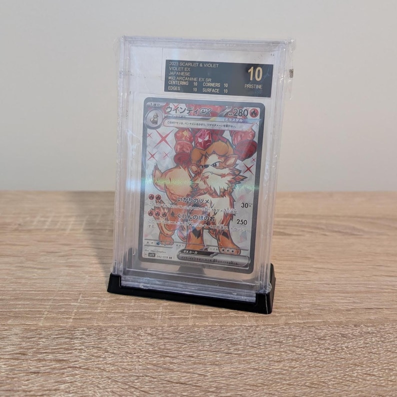 May include: A graded Pok&eacute;mon card in a clear protective case. The card features a detailed illustration of a fiery, canine-like creature. The card is graded a 10, with text in Japanese and English.