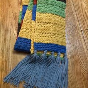 May include: A multi-colored striped crocheted scarf with blue tassels. The scarf has stripes of yellow, green, brown, red, and blue.