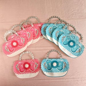 Peut inclure: Un ensemble de dix sacs de fête, cinq roses et cinq bleus, avec une bordure de perles et un nœud. Les sacs sont en forme de sacs à main et ont une poignée.