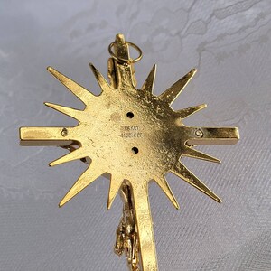 May include: A gold-toned crucifix pendant with a sunburst design. The back of the cross features the text "CAART - MOLDED". The crucifix depicts a detailed figure of Jesus Christ.
