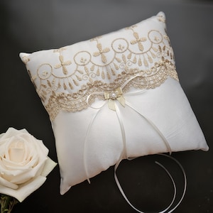 May include: White satin ring pillow with gold lace trim and a satin ribbon bow with a pearl accent.