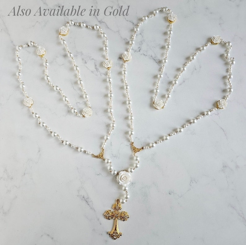 May include: White pearl rosary necklace with a gold cross and white rose accents. Also Available in Gold.