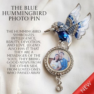 May include: A blue hummingbird photo pin with a clear round photo frame. The hummingbird is decorated with rhinestones and has a white and blue enamel finish. The photo frame has a silver border and is attached to the hummingbird by a silver chain. The pin is new and has a red and white "NEW" label.