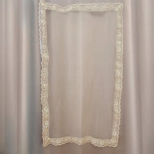 Puede incluir: Un rect&aacute;ngulo de tela blanca transparente con un borde de encaje blanco.
