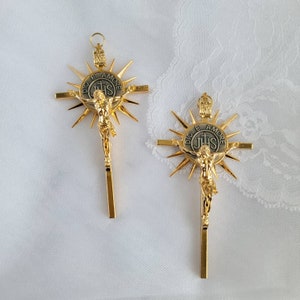 May include: Two gold-colored crucifix pendants. Each features a detailed depiction of Jesus Christ on the cross, with a sunburst design behind the cross. The center of the cross has the text "DIO E AMORE" and "IHS".