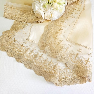 May include: A delicate, sheer, ivory tablecloth with a gold lace trim. The lace features a repeating pattern of circles and floral motifs.