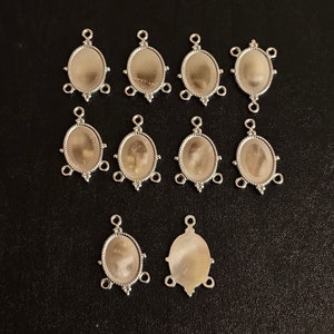May include: Ten silver-toned metal pendant settings with oval-shaped bezels and three loops on each side. The settings are designed for adding a cabochon stone or other embellishment.