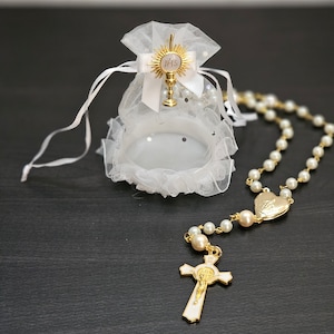 Peut inclure: Un sac en organza blanc avec un emblème de calice doré et un chapelet de perles. Le sac a une fermeture à ruban et une bordure à volants. Le chapelet comporte de fausses perles et un pendentif en croix doré.