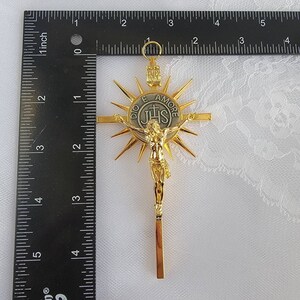 May include: A gold-colored crucifix with a sunburst design behind the figure of Jesus. The cross is approximately 4 inches long. The center medallion reads "DIO E AMORE" and "IHS".